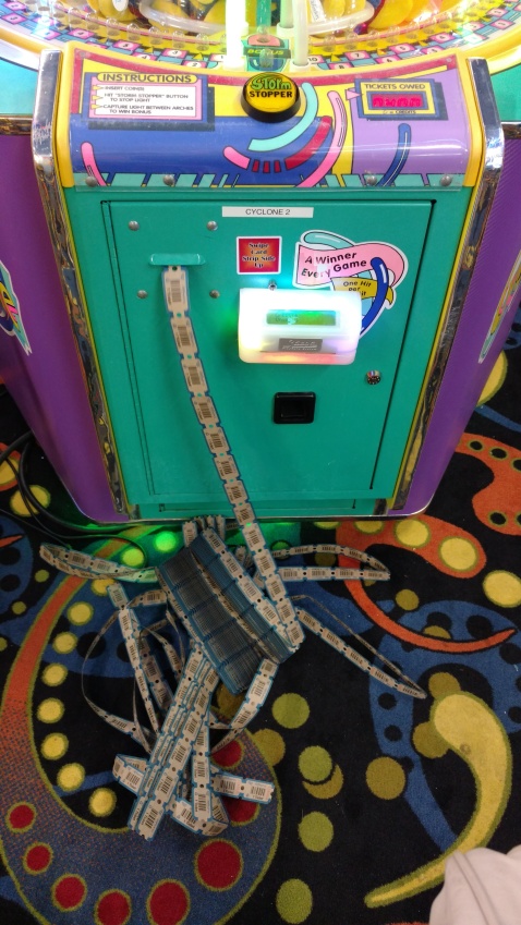The floor in front of a ticket game in an arcade with a large pile of tickets coming out of a machine.